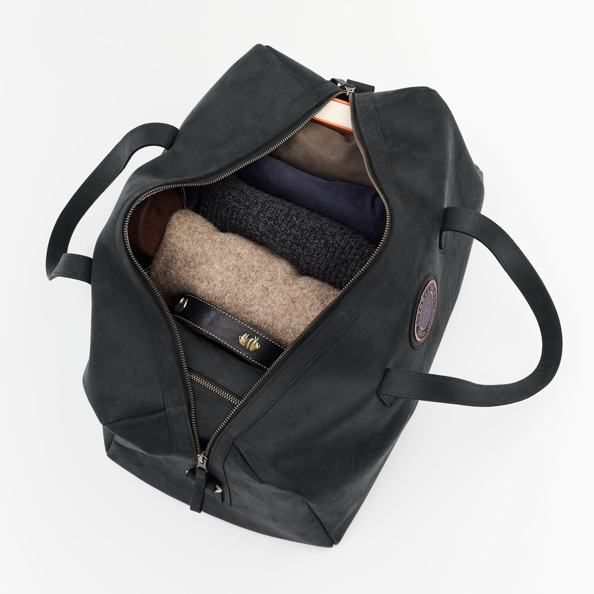 An open black leather duffel bag with clothes inside on a white background
