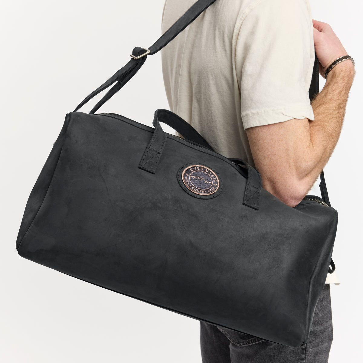 Person holding a black leather duffel bag with the Everwest brand logo on a light gray background