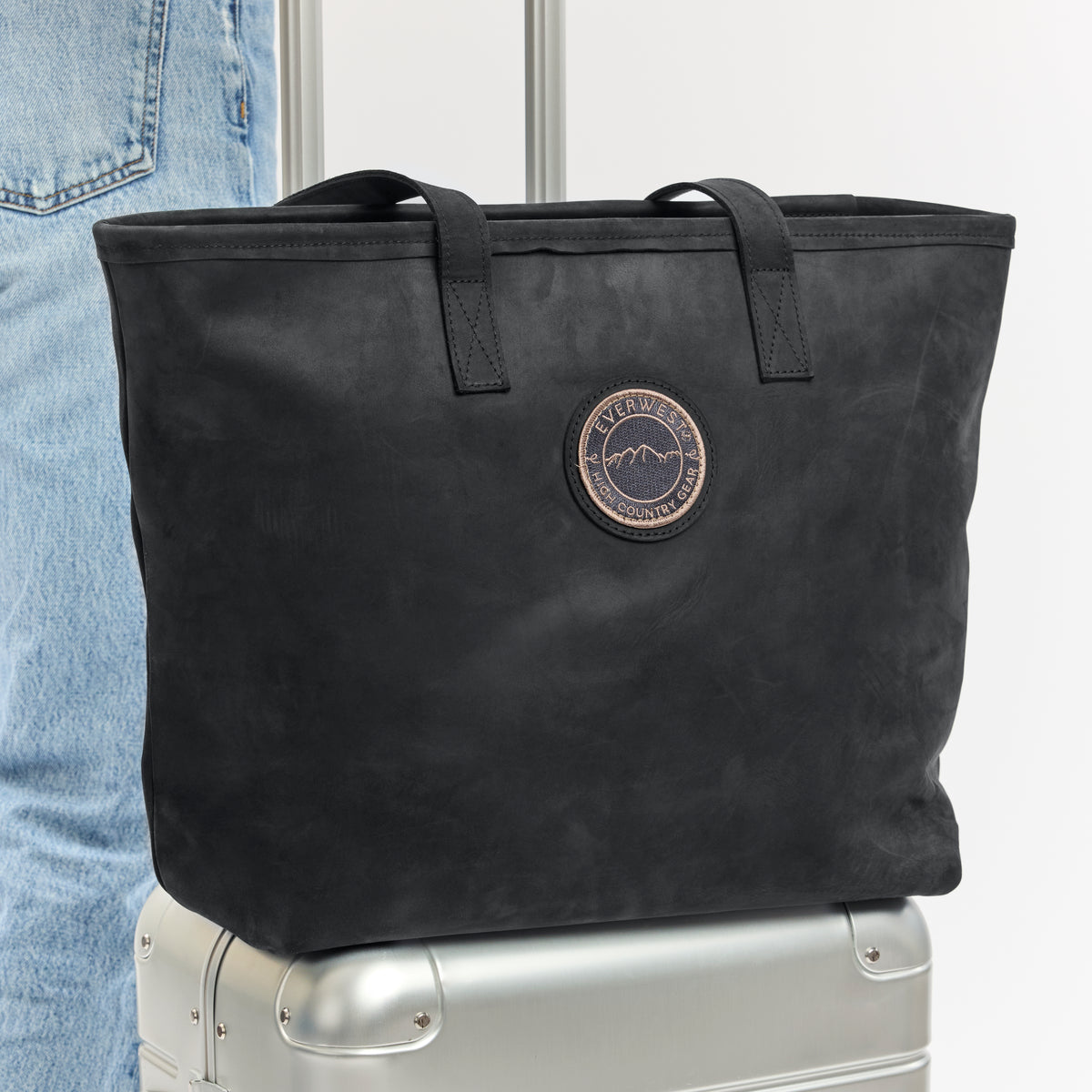 Black leather tote bag with the Everwest patch logo on a silver suitcase