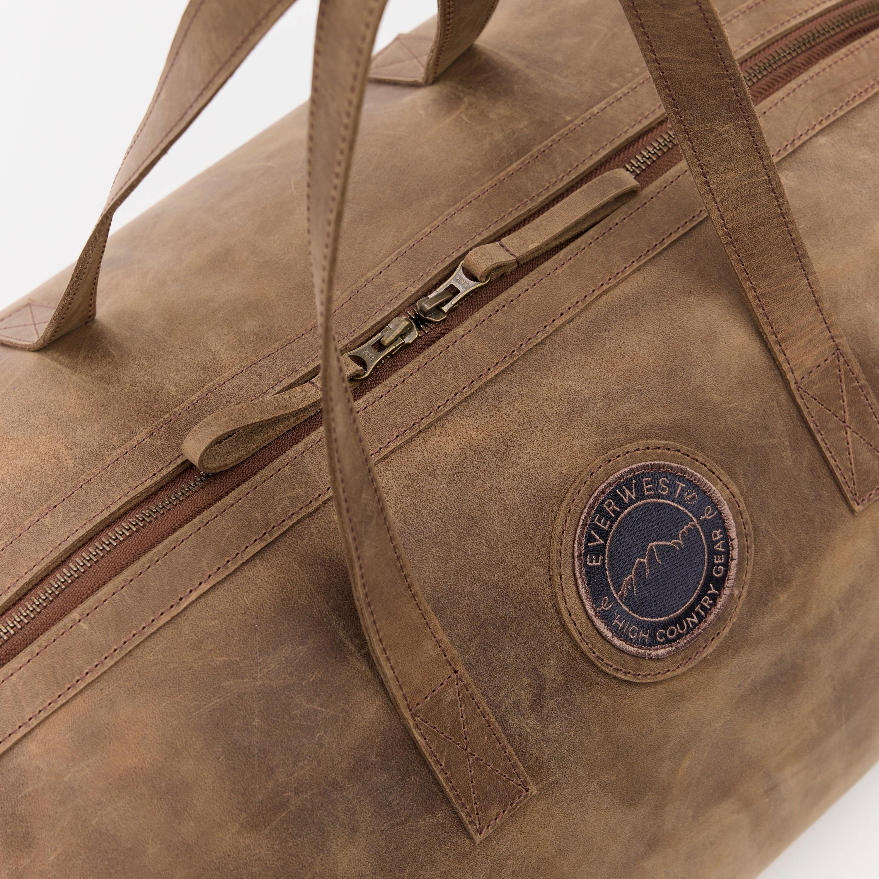 Brown leather duffel bag with a visible brand logo on a light gray background