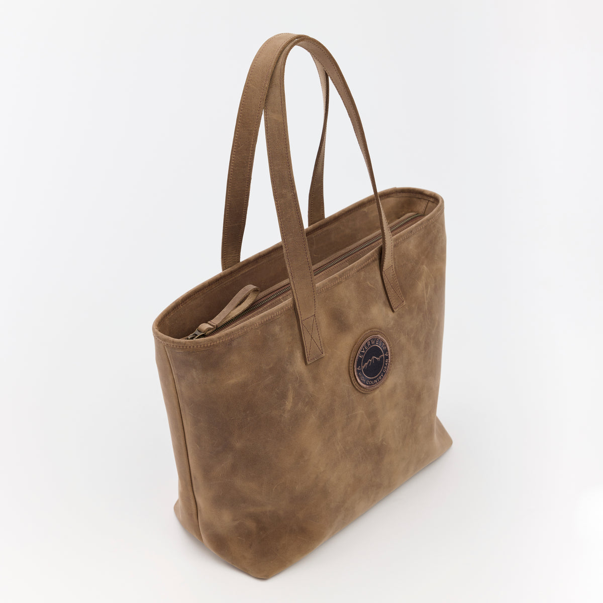 Brown leather tote bag with the Everwest brand logo patch on a white background
