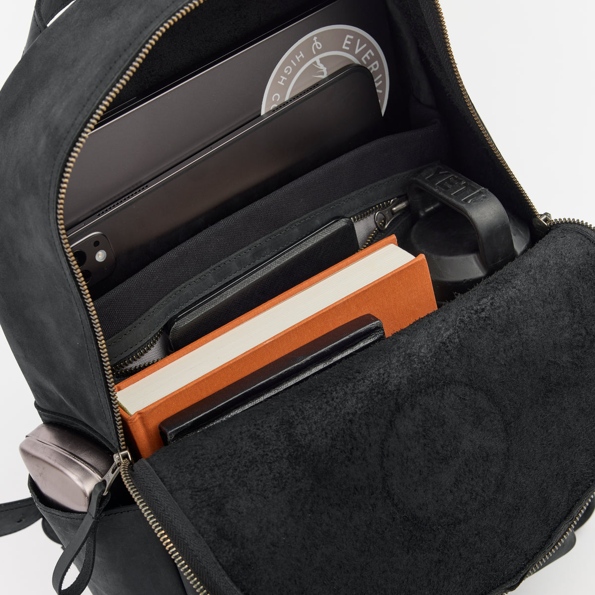 Black leather backpack with compartments containing a tablet and other items on a white background