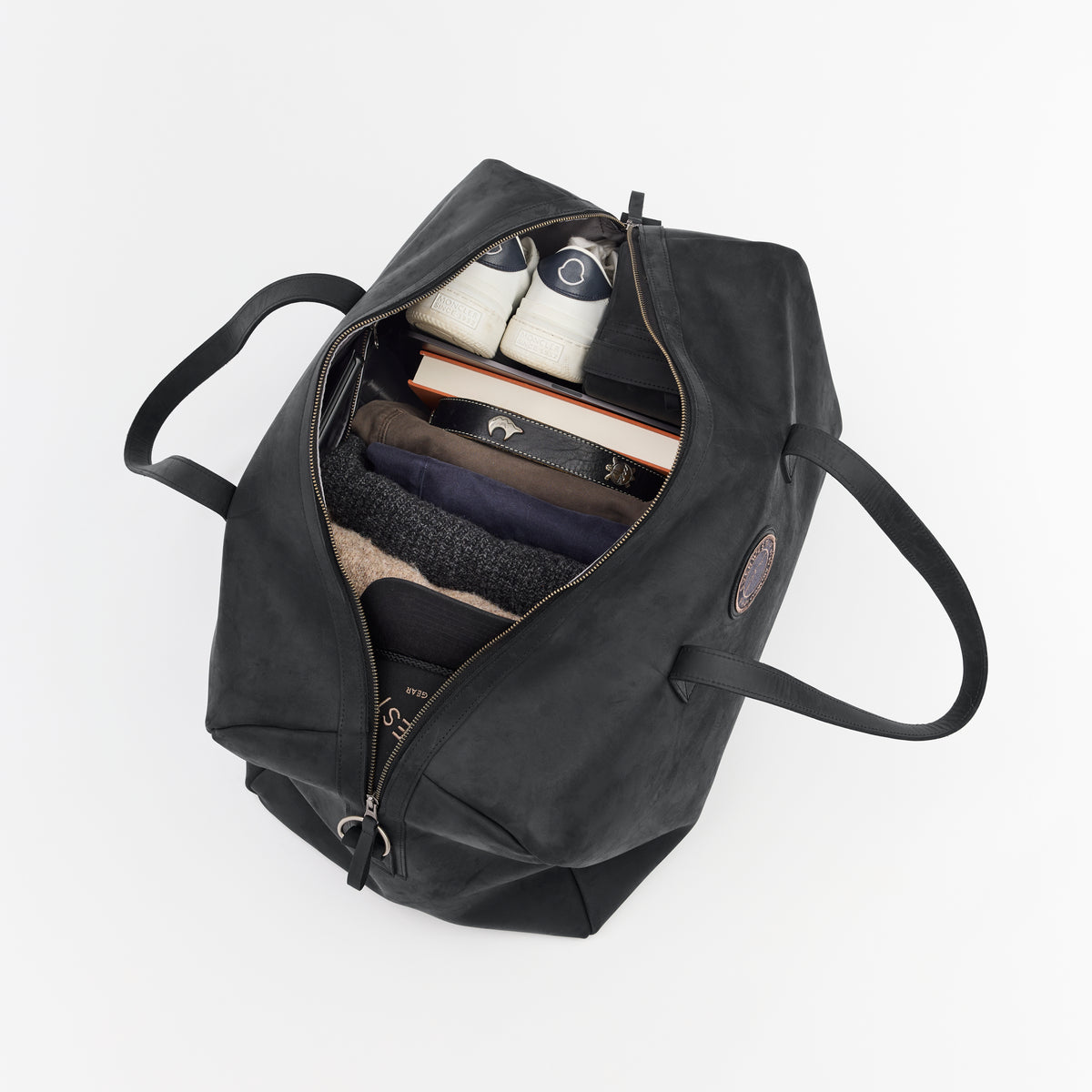 Large black leather duffel bag with items inside on a white background