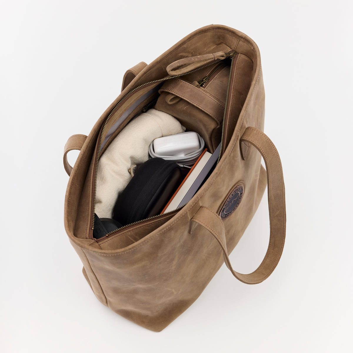 Brown leather bag with items inside a zippered compartment on a white background