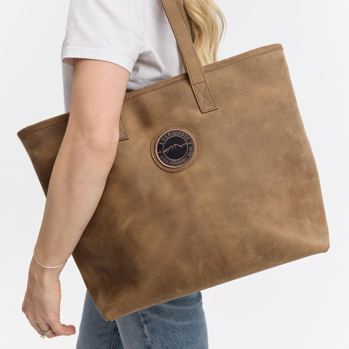 Brown leather tote bag with the Everwest brand logo held by a person on a white background
